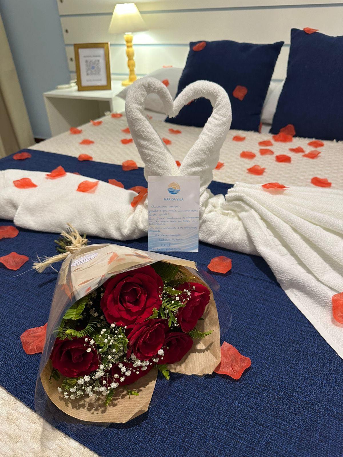 Decoração romântica com cisnes de toalha em coração, buquê de rosas e cartão personalizado sobre a cama