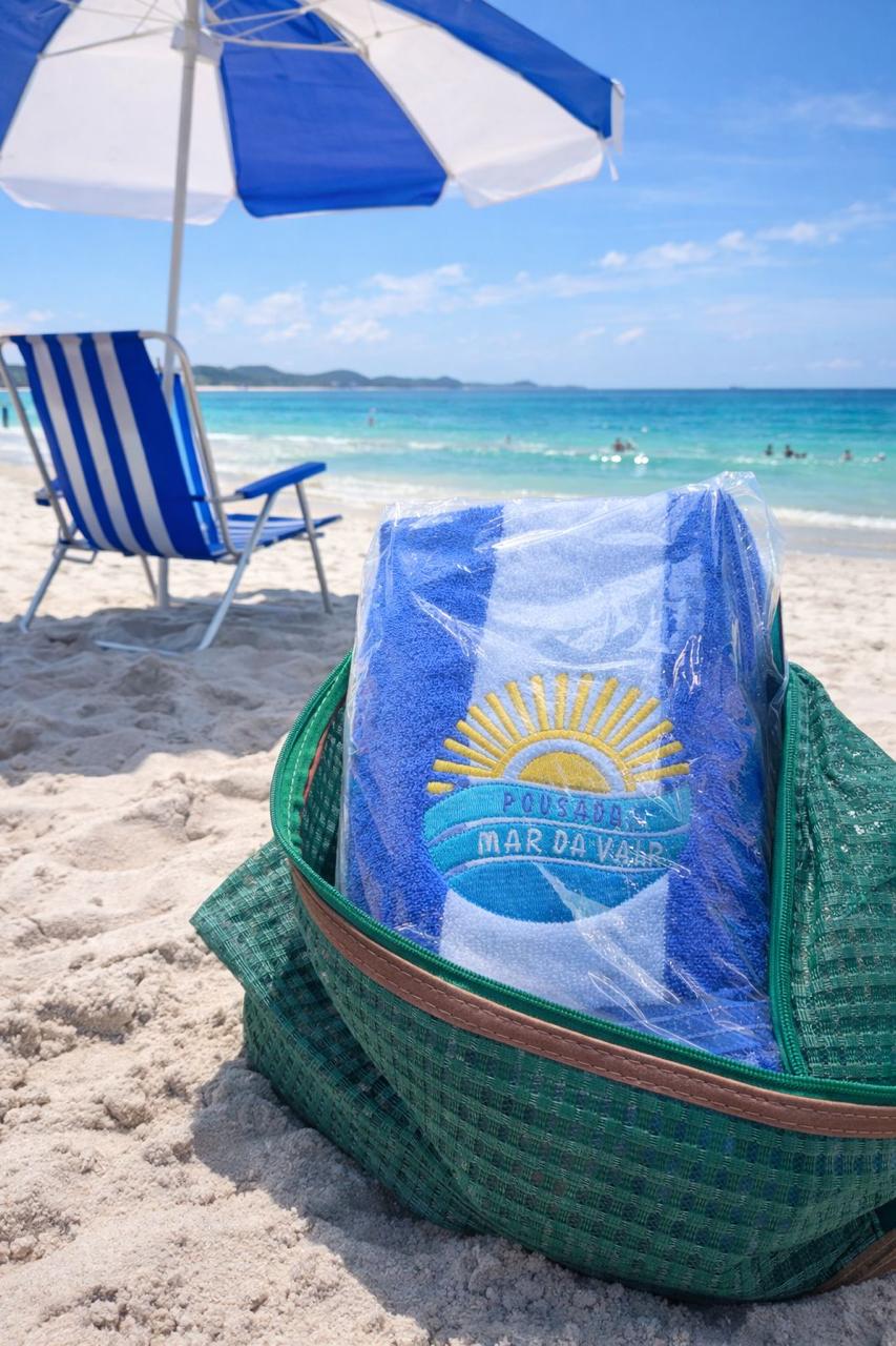 Toalha de praia personalizada com a logo bordada da Pousada Mar da Vila, dentro de bolsa térmica verde, na areia da praia